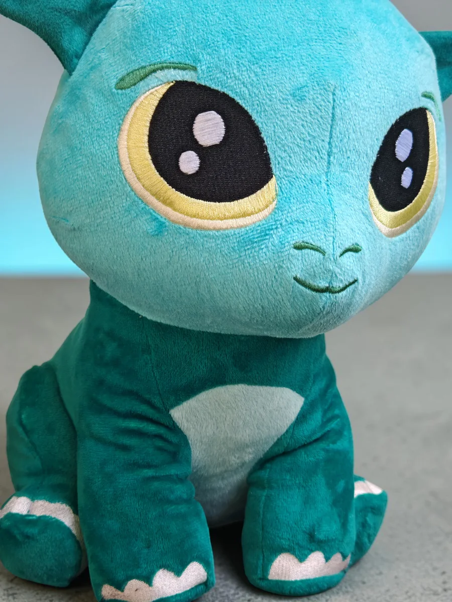 Kobi, le dragon Playnitive vert turquoise, photographié en gros plan, avec de grands yeux brodés