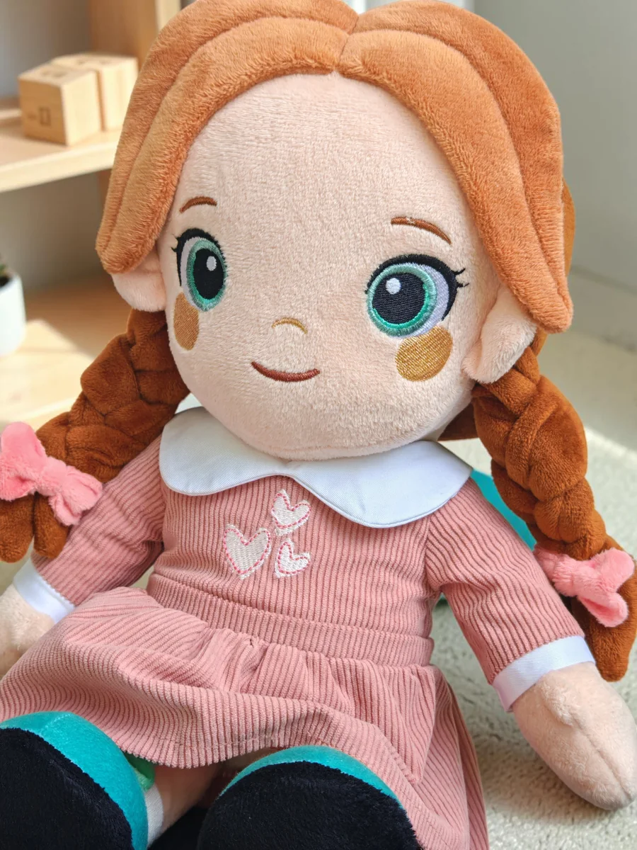 Lotti, la poupée Playnitive, photographiée en gros plan : tresses auburn, yeux brodés et robe rose en velours côtelé
